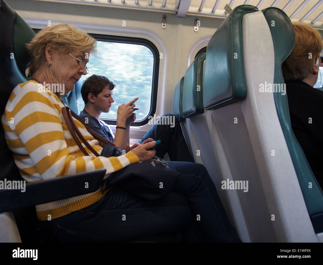 Senior donna e giovane uomo che utilizza smartphone su un treno dei pendolari in New York, Stati Uniti d'America, 30 maggio 2014, © Katharine Andriotis Foto Stock