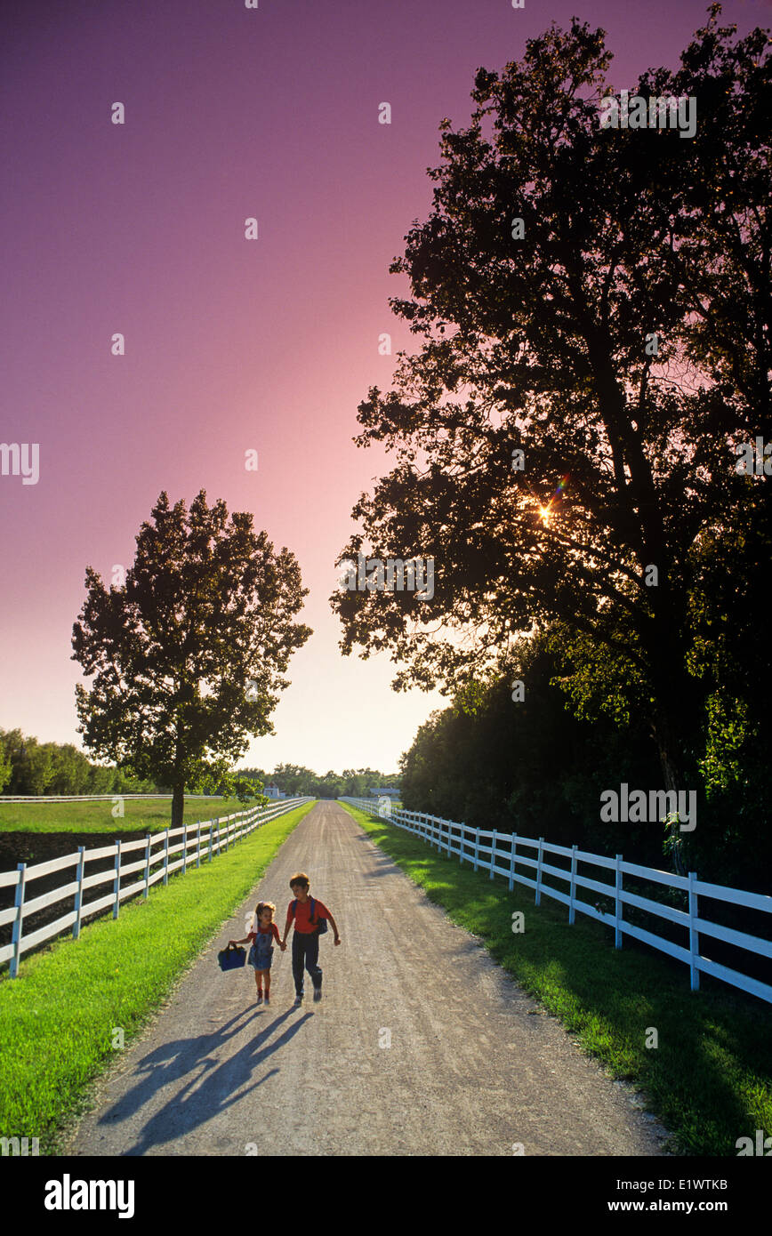 Due bambini correre giù per una strada di campagna sulla loro strada per la scuola, nei pressi del Grande Pointe, Manitoba, Canada Foto Stock