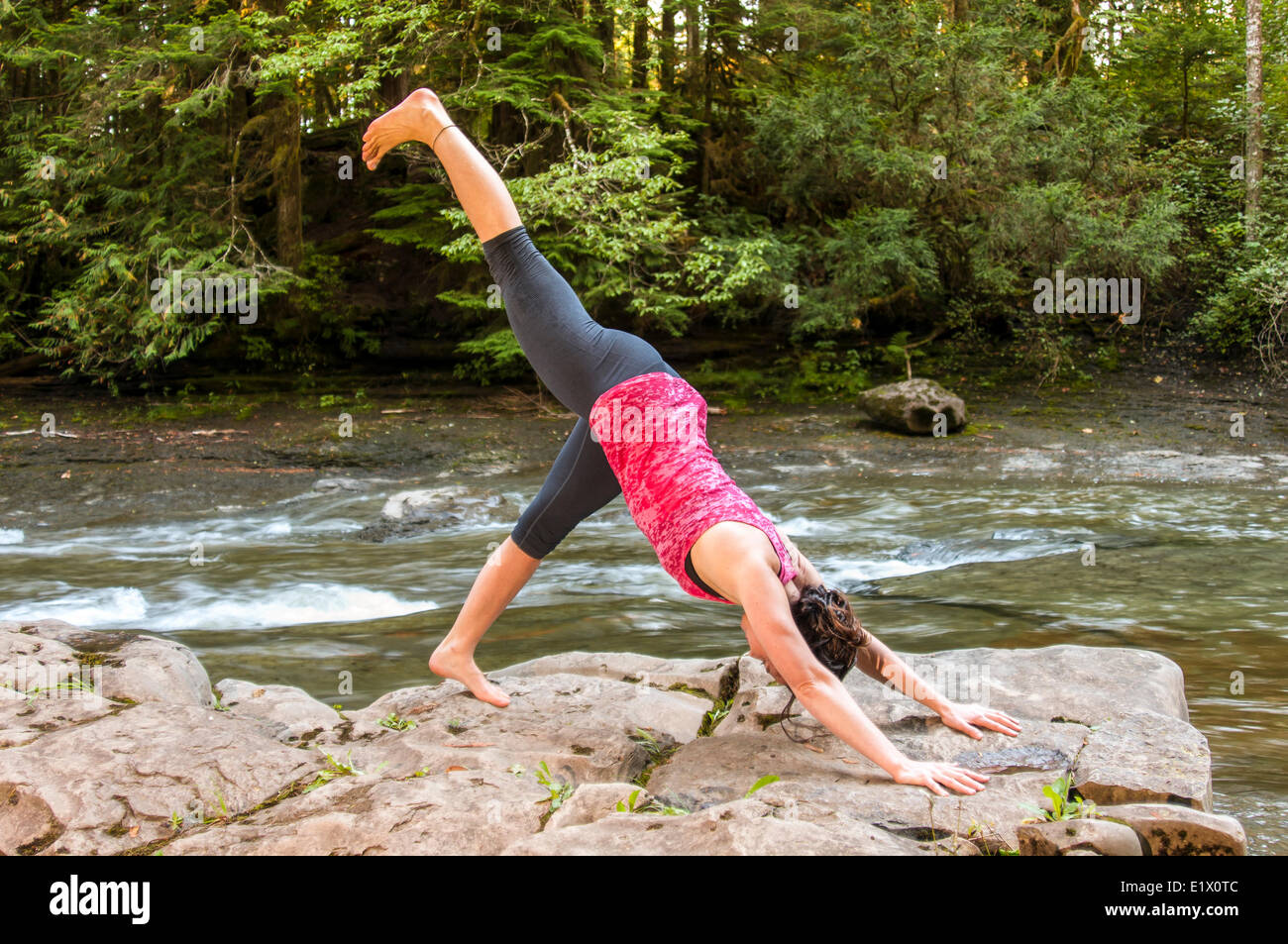 Posizione del Cane con la testa in giù; Cane su tre zampe, yoga pone all'aperto nella parte anteriore di un fiume, Courtenay, British Columbia, Canada Foto Stock