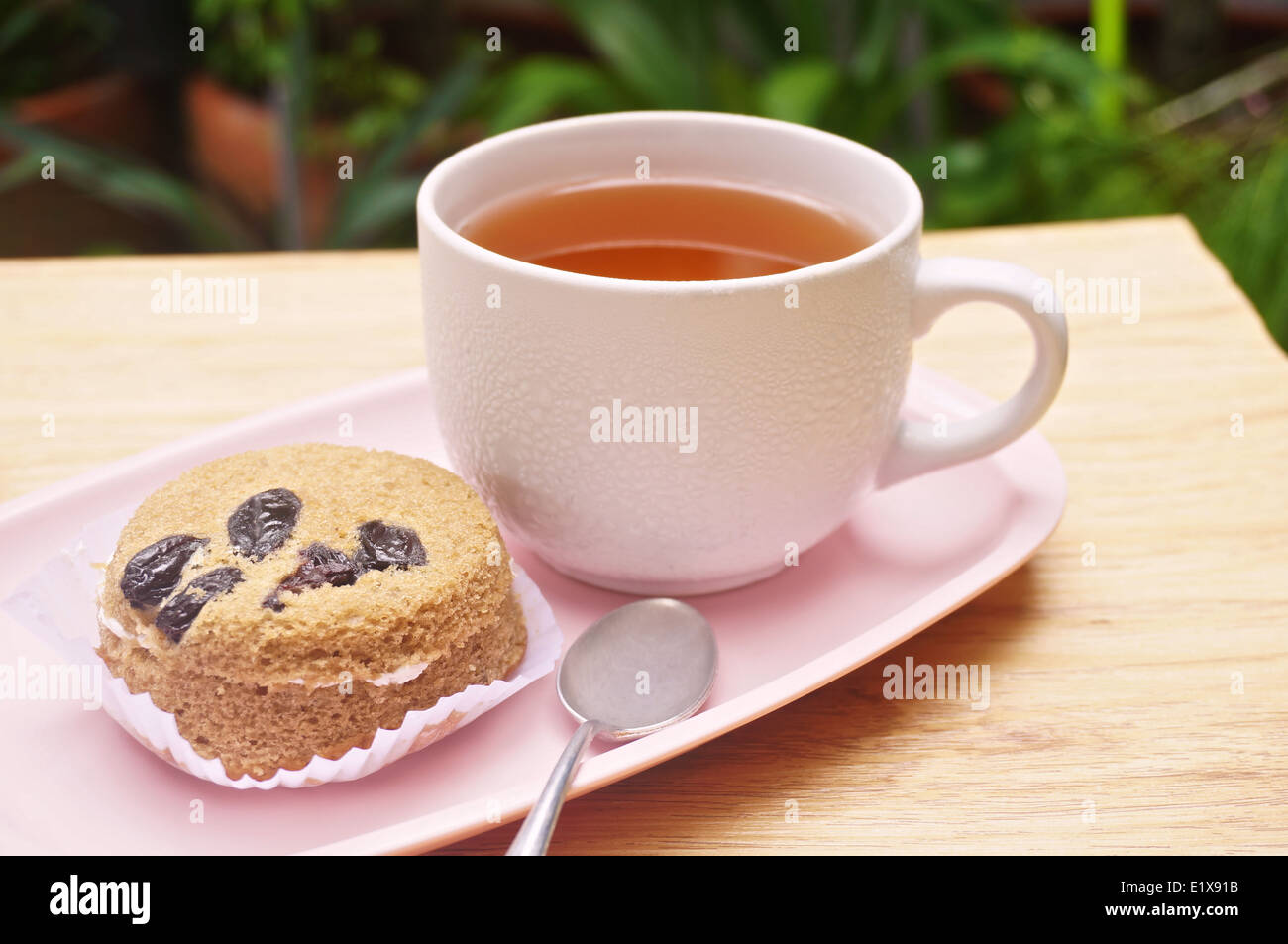 Il tè in tazza bianca e torta al lato con cucchiaio messo sul vassoio rosa in giardino. Foto Stock