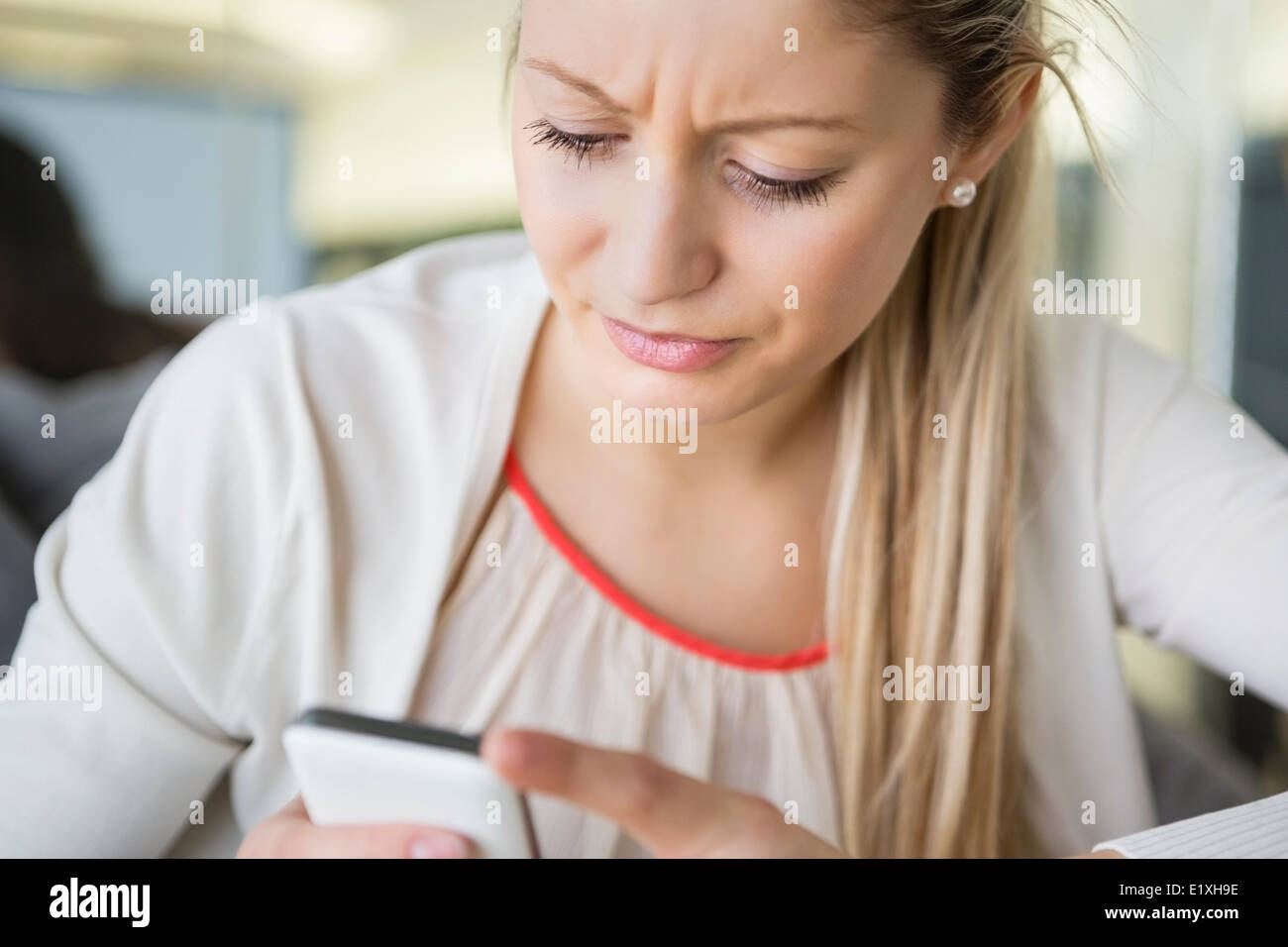Giovane imprenditrice della messaggistica di testo tramite telefono cellulare in ufficio Foto Stock