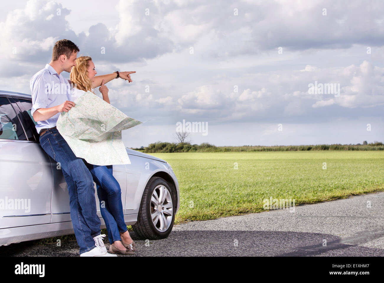 Lunghezza completa di coppia con mappa discutendo di direzione mentre appoggiato su auto in campagna Foto Stock