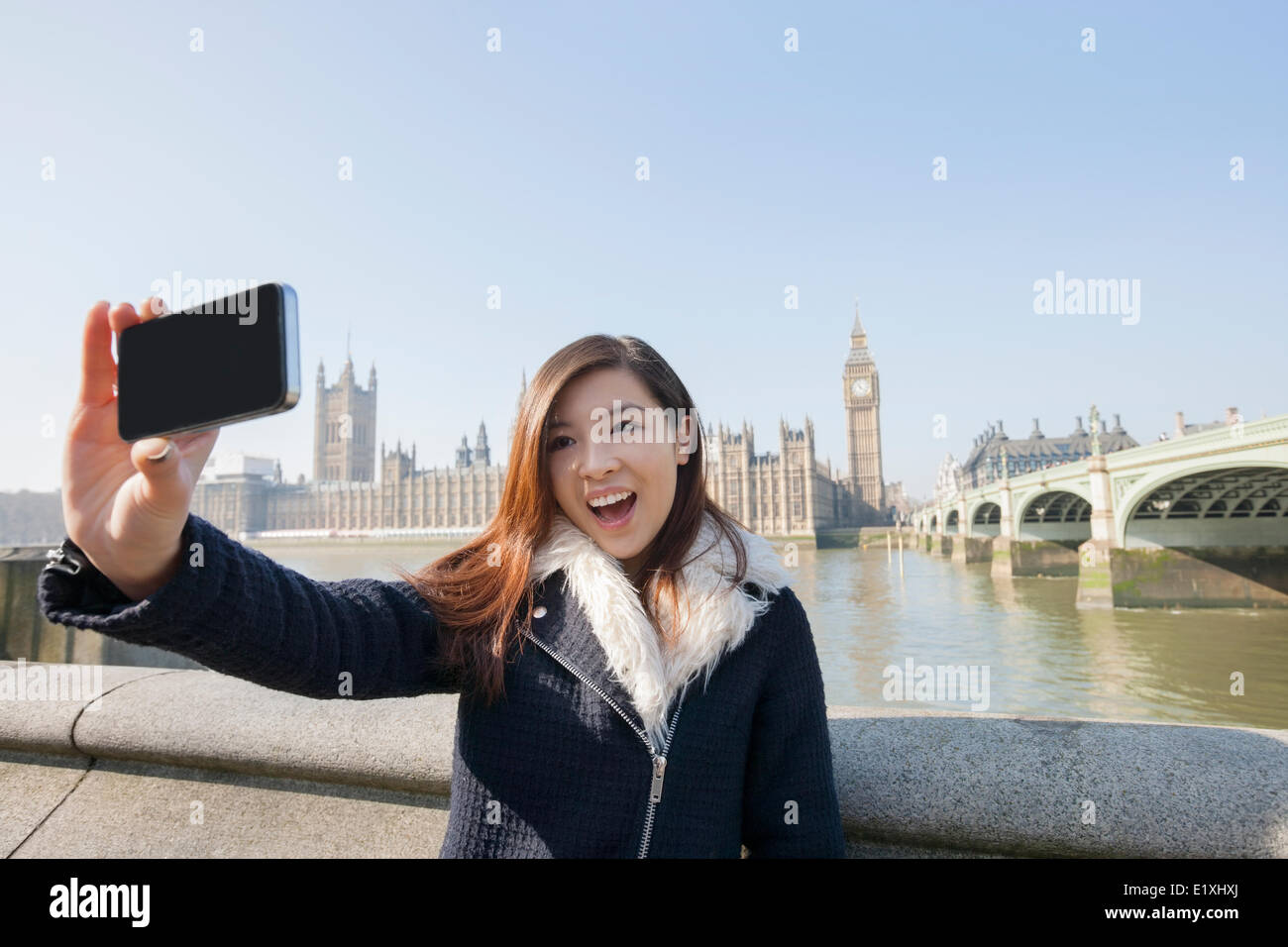 Felice giovane donna prendendo ritratto di auto attraverso il telefono cellulare contro il Big Ben a Londra, Inghilterra, Regno Unito Foto Stock