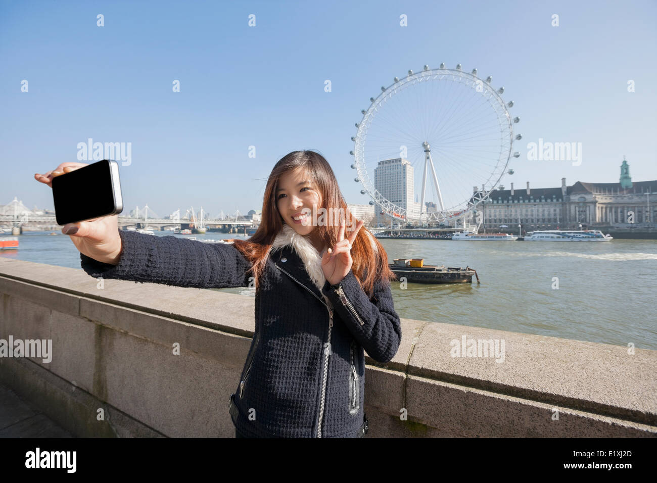 Donna felice tenendo ritratto di auto attraverso il telefono cellulare contro il London Eye a Londra, Inghilterra, Regno Unito Foto Stock