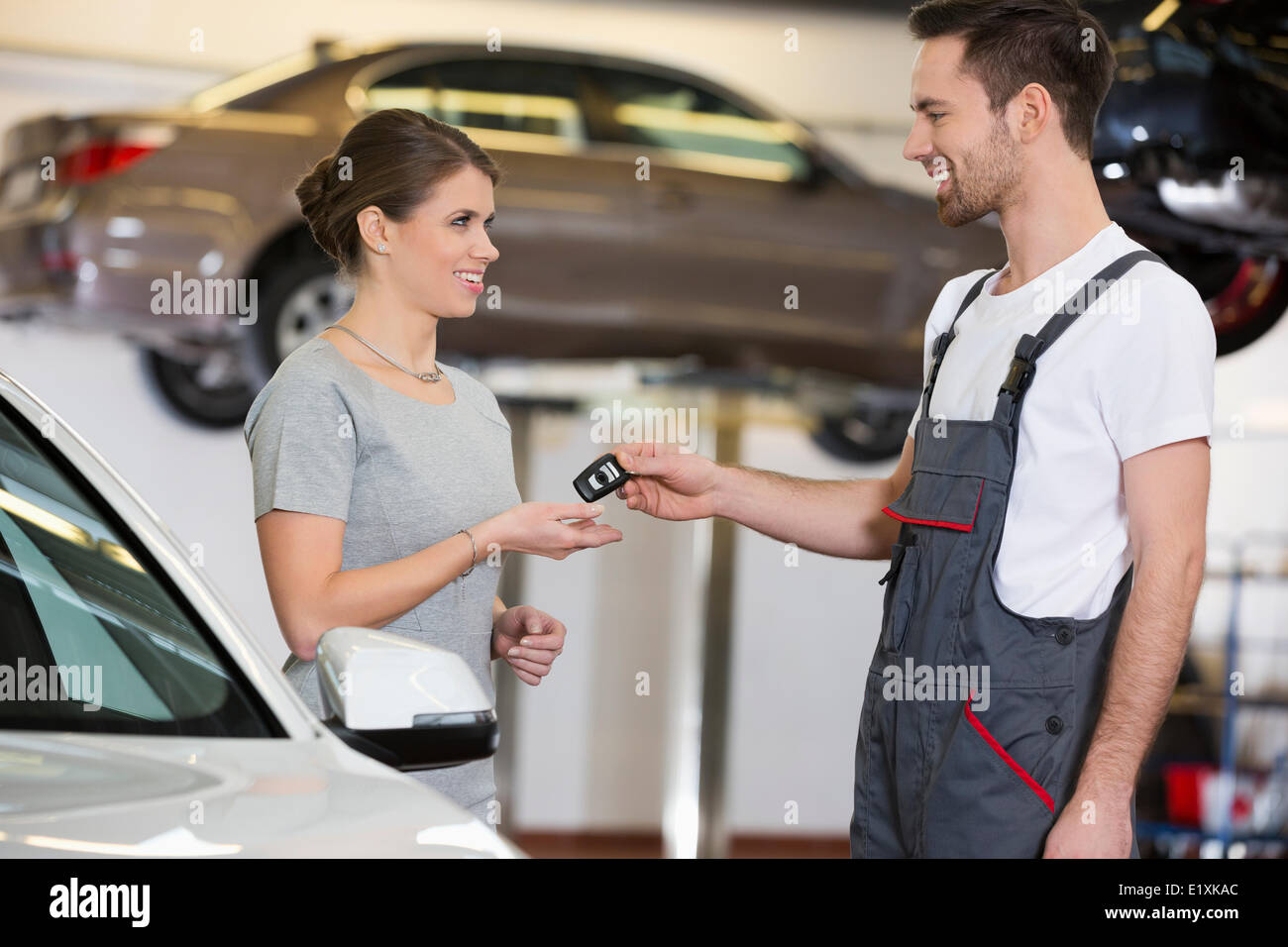 Felice repairman dando chiave auto per donna in officina Foto Stock