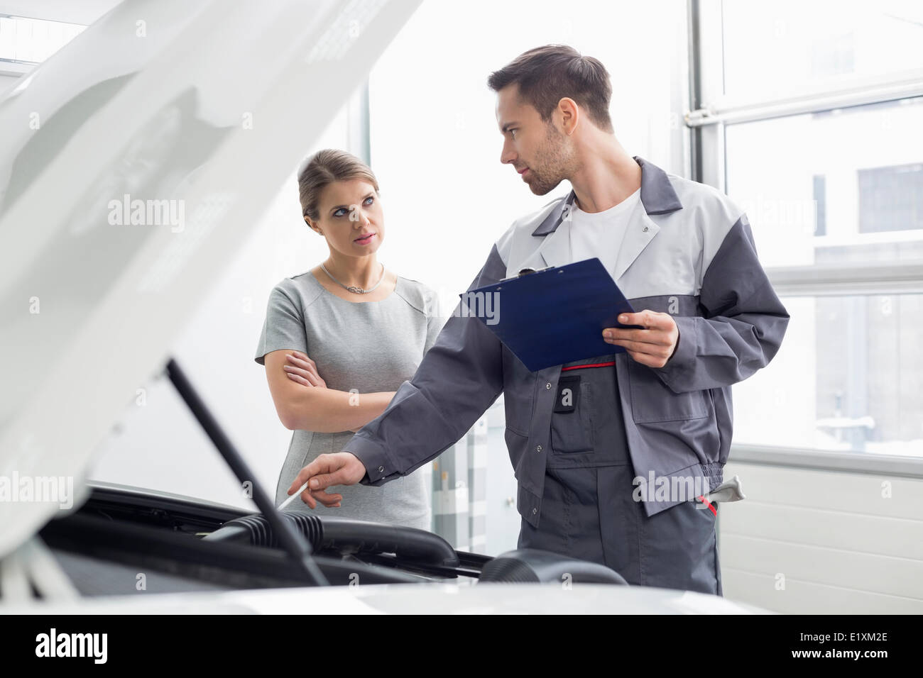 Giovane ingegnere maschio spiegando auto motore a femmina cliente in officina Foto Stock