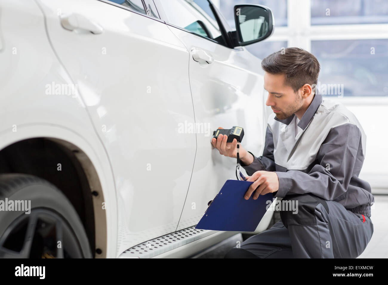 Riparazione maschio lavoratore esaminando la vernice dell'auto con Attrezzature per officina di riparazione Foto Stock