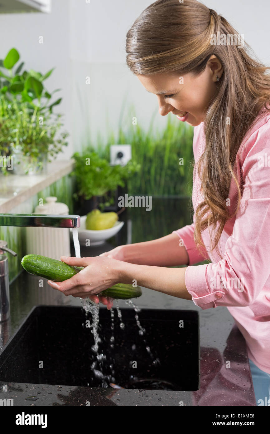 Donna sorridente il lavaggio di cetriolo in cucina Foto Stock