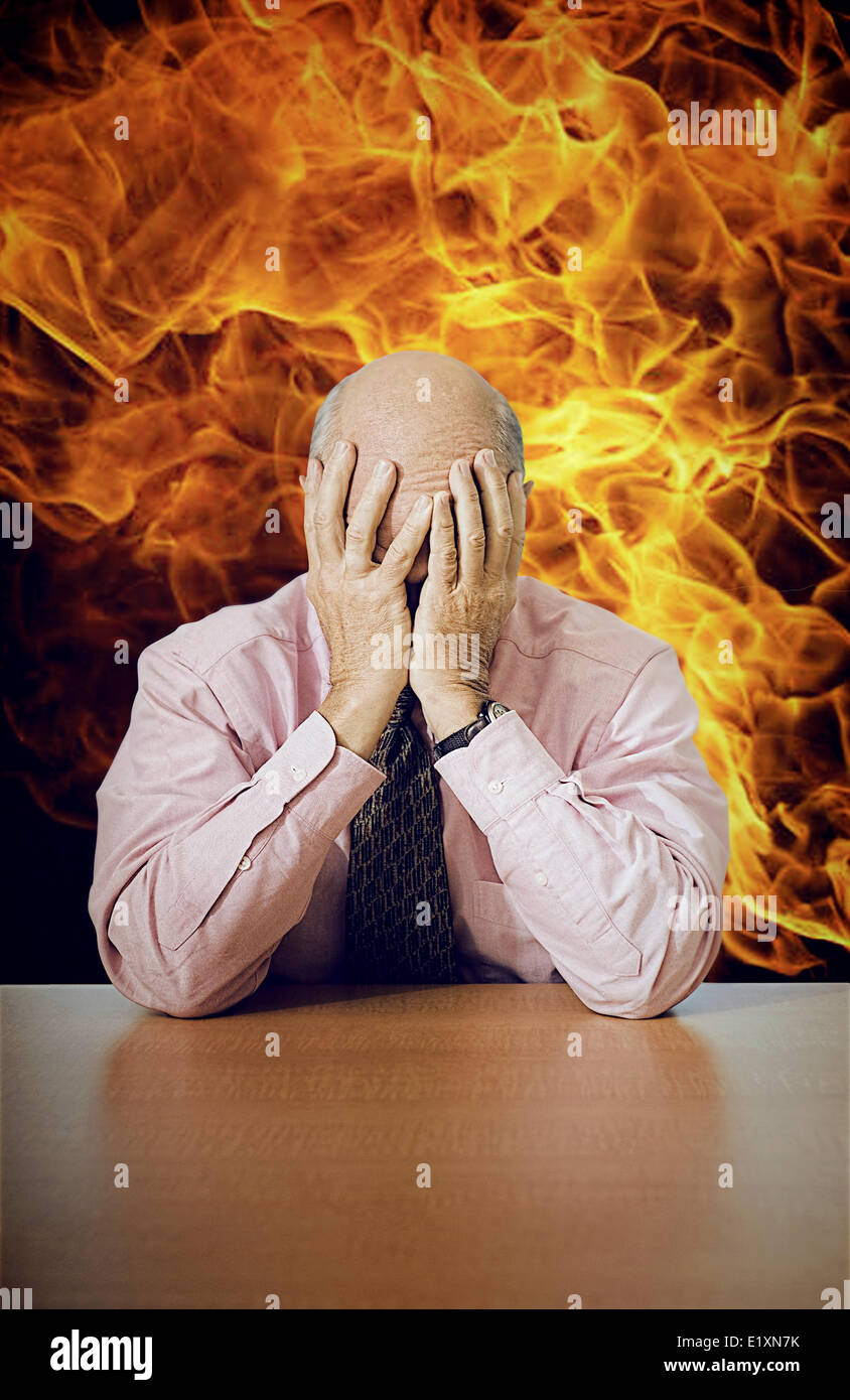 Premuto imprenditore senior seduto alla scrivania con il fuoco in background Foto Stock