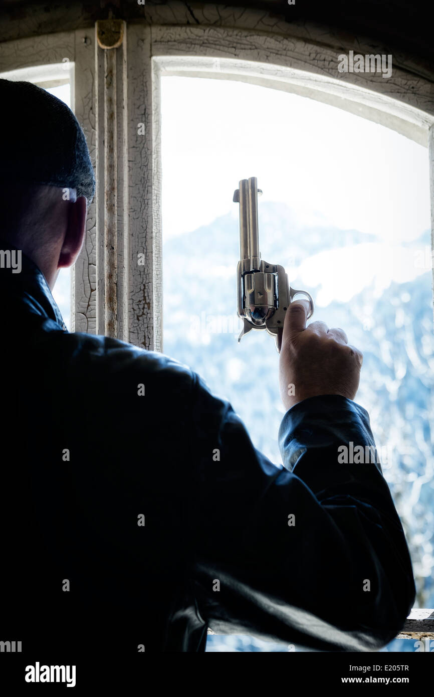 Un uomo con una pistola di fronte a una vecchia finestra in un edificio abbandonato Foto Stock