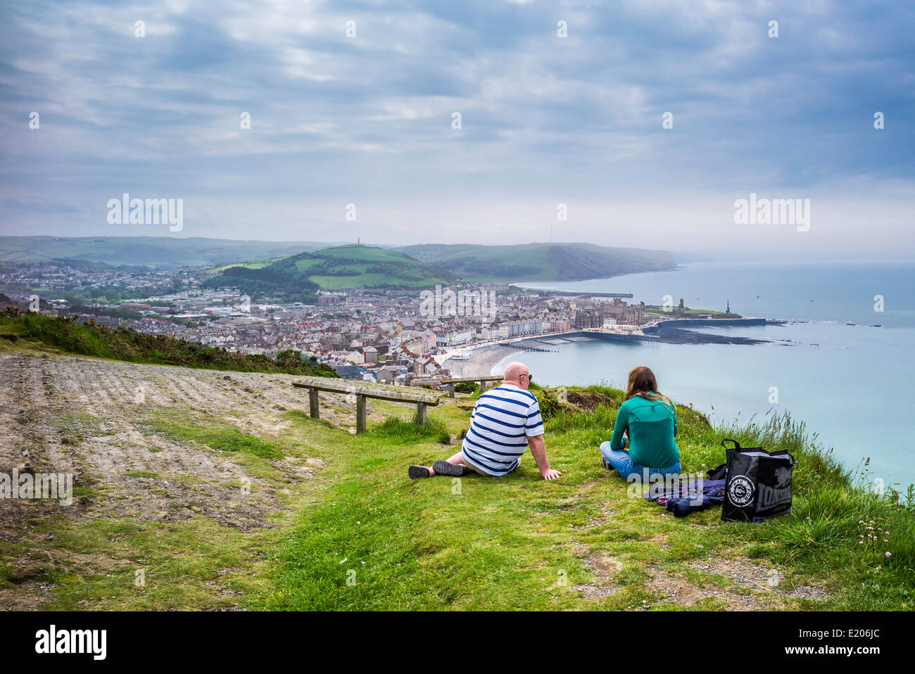 Coppia matura, maschio e femmina di sedersi sull'erba alla sommità della collina di costituzione Aberystwyth affacciato su Cardigan Bay Foto Stock