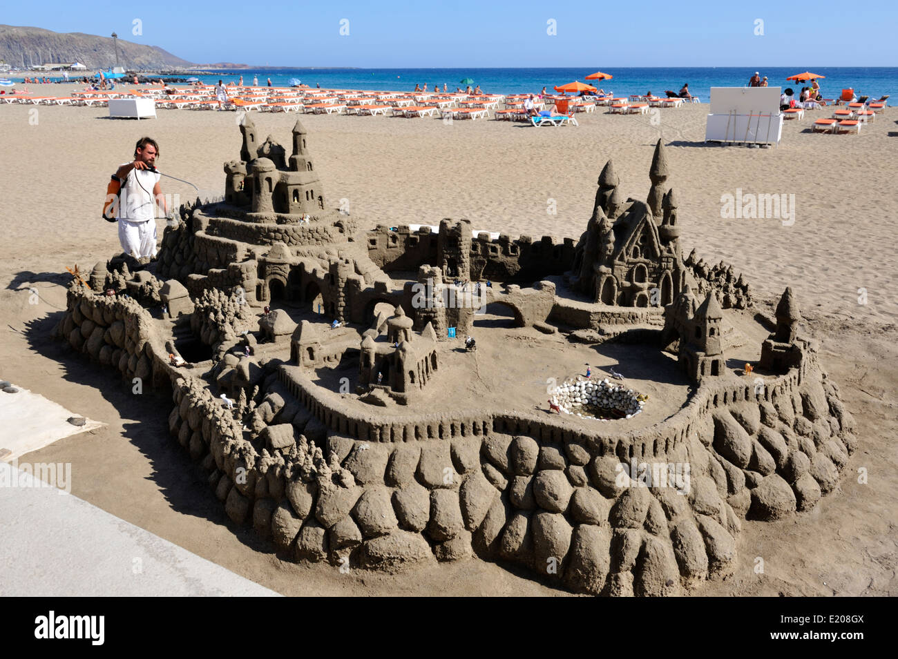 Castello di sabbia sulla spiaggia di Tenerife con scultore tendente da mantenerlo umido Foto Stock