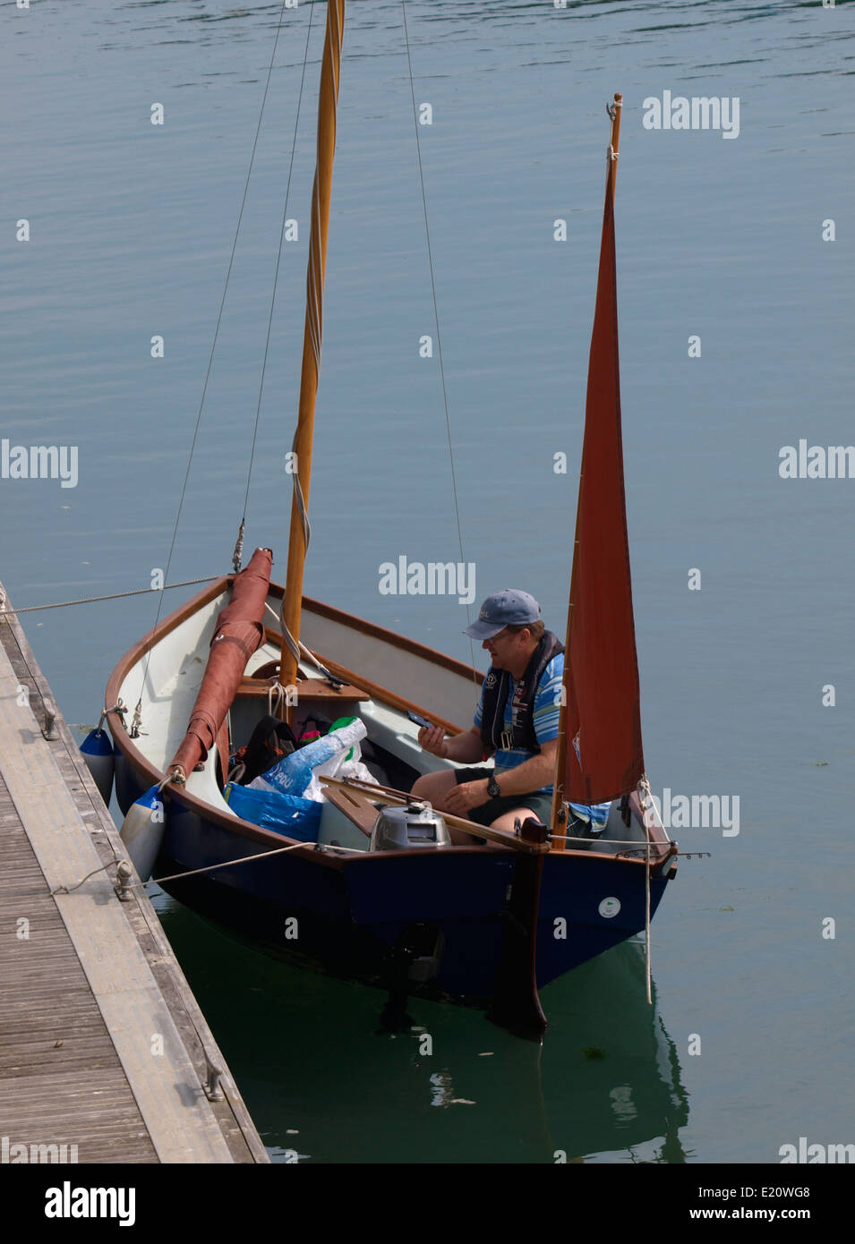 L'uomo la preparazione di discostarsi in una piccola barca a vela con vele rosso, Padstow, Cornwall, Regno Unito Foto Stock