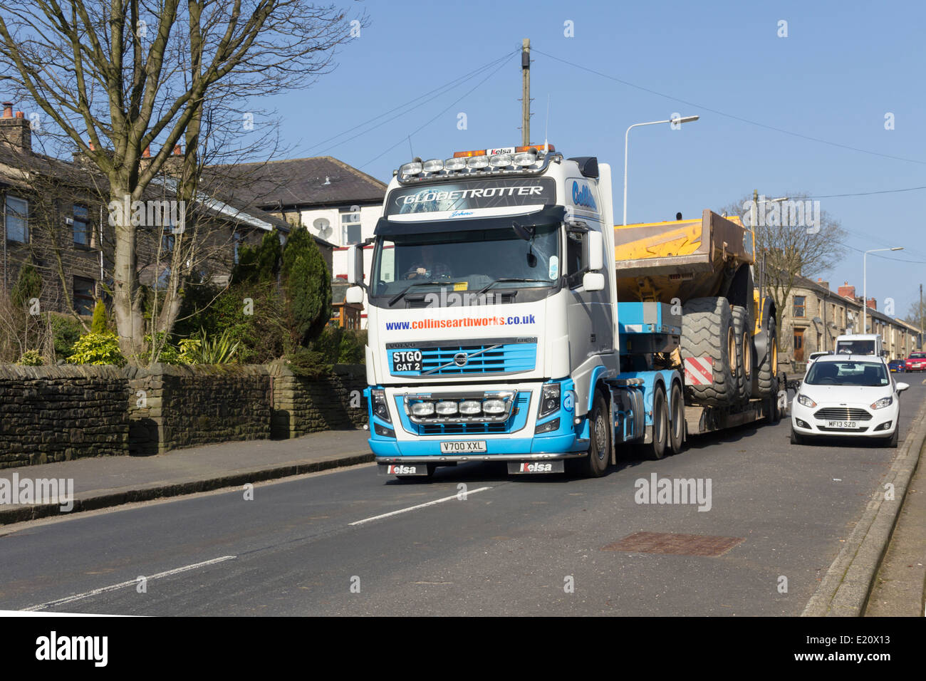 Ampia-carico, movimento terra camion vengono trasportati su una Volvo FH16 bassa-caricatrice attraverso un villaggio nel nord-ovest dell'Inghilterra. Foto Stock