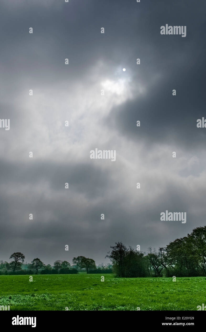 Sun attraverso dense nuvole grigie sulla campagna inglese; orientamento verticale. Foto Stock