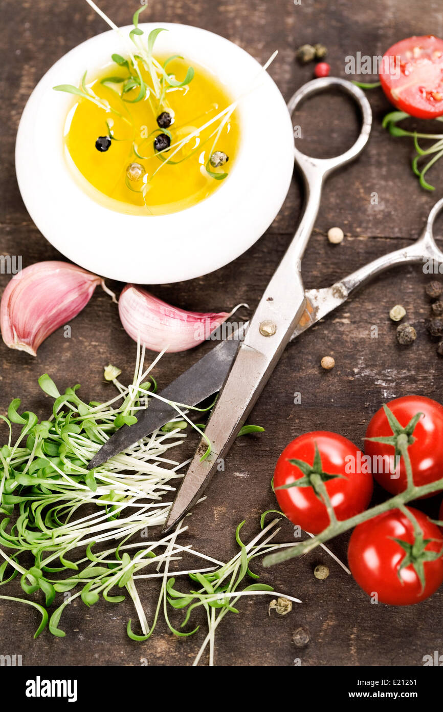 I germogli, aglio, pomodori, olio di oliva e un paio di forbici sul vecchio tavolo da cucina Foto Stock