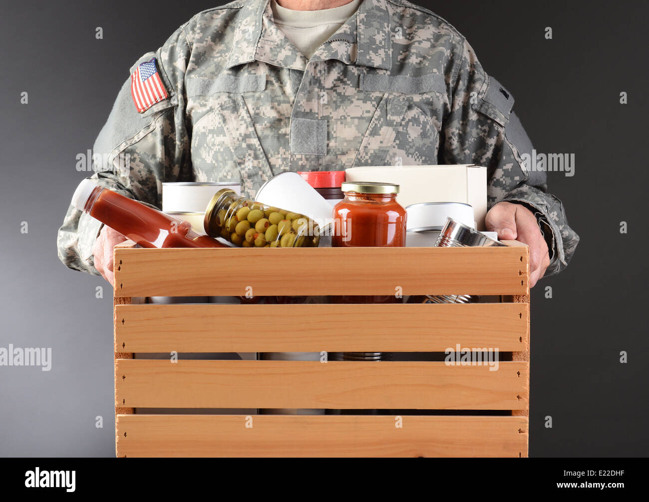 Primo piano di un soldato in fatiche in possesso di una scatola di legno piena di conserve e alimenti confezionati per una vacanza carità drive. Foto Stock
