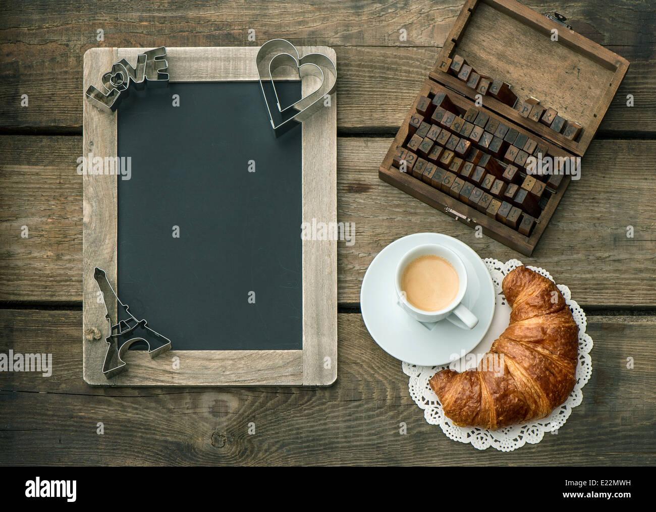 Tazza di caffè nero con croissant, lavagna e decorazione di cuore in legno rustico sfondo. Foto Stock