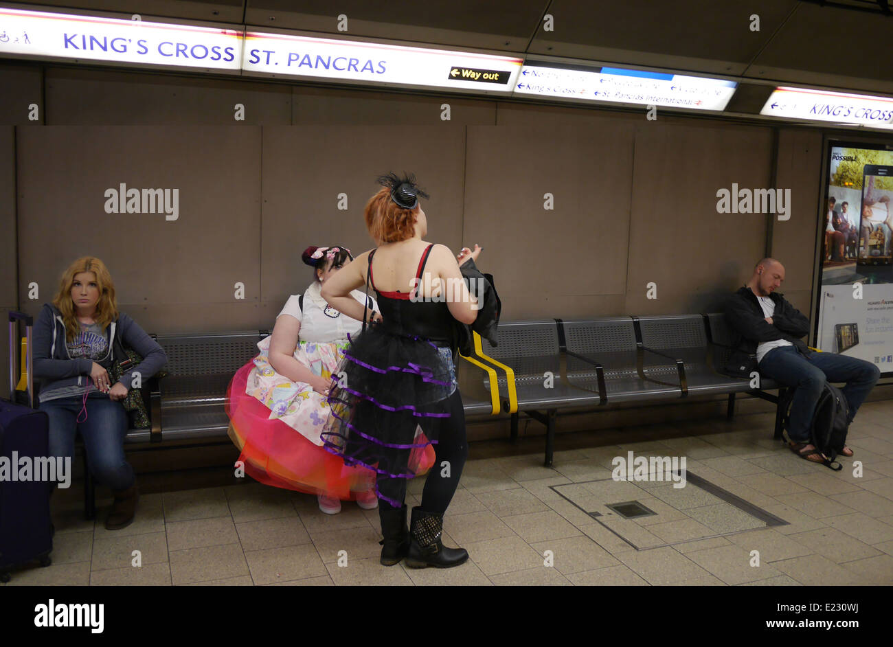 Ragazze in costumi cosplay in attesa sul binario con passeggeri in una stazione della metropolitana di Londra, Regno Unito. Foto Stock