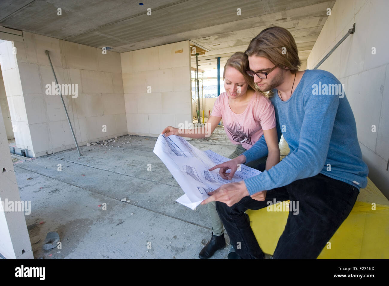 Coppia giovane con blueprint sta cercando nel soggiorno come la loro nuova casa è in fase di costruzione Foto Stock