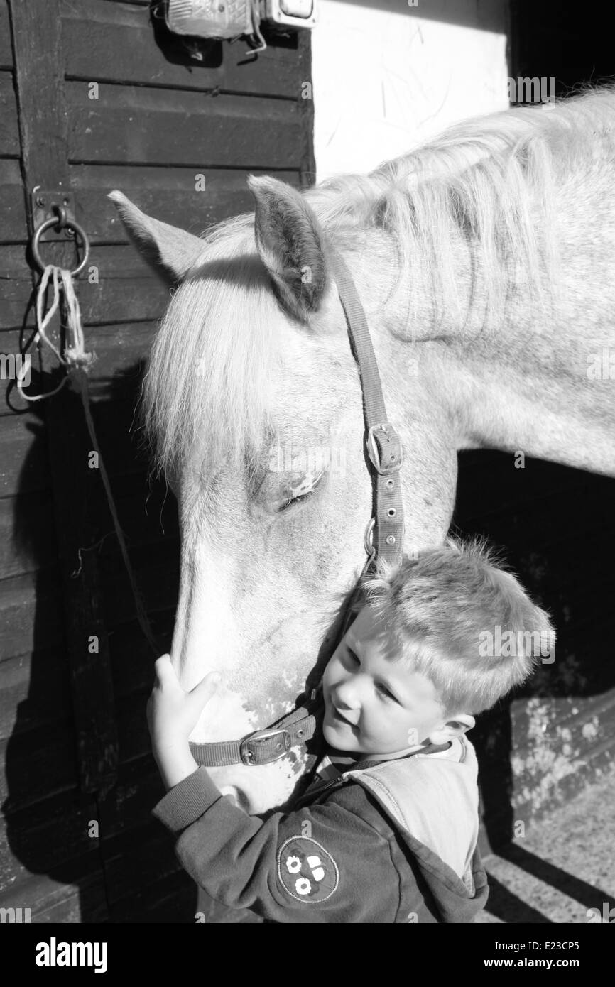 Piccolo Ragazzo dando il suo cavallo preferito un abbraccio. Foto Stock