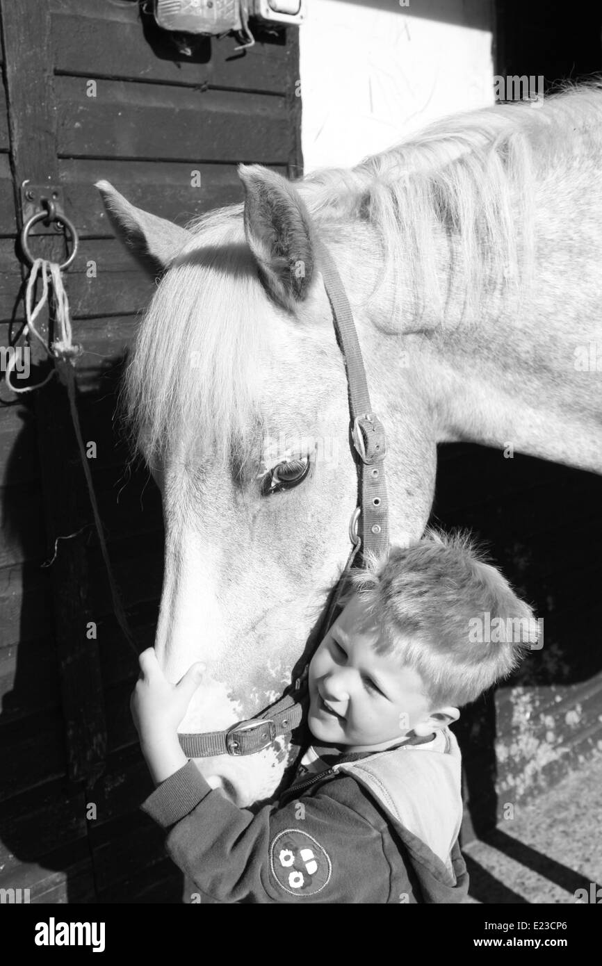 Piccolo Ragazzo dando il suo cavallo preferito un abbraccio Foto Stock