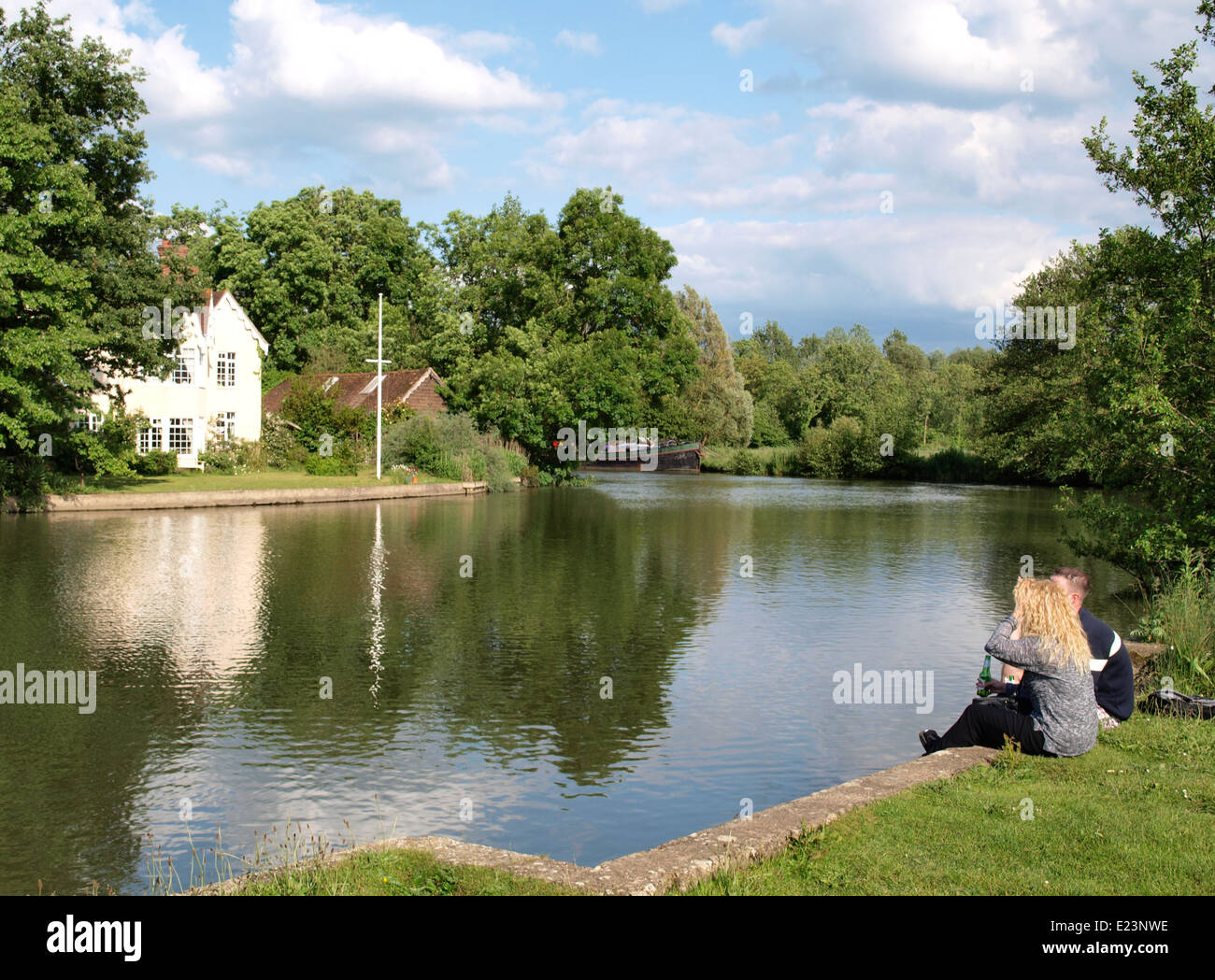 Giovane seduto sul greto del fiume gustando una birra in una serata estiva, Fiume Tamigi vicino a Oxford, Regno Unito Foto Stock