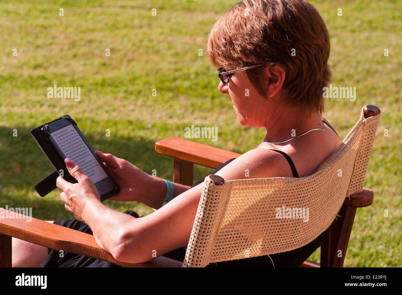Una donna di mezza età seduta fuori nel sole la lettura di un libro e Foto Stock