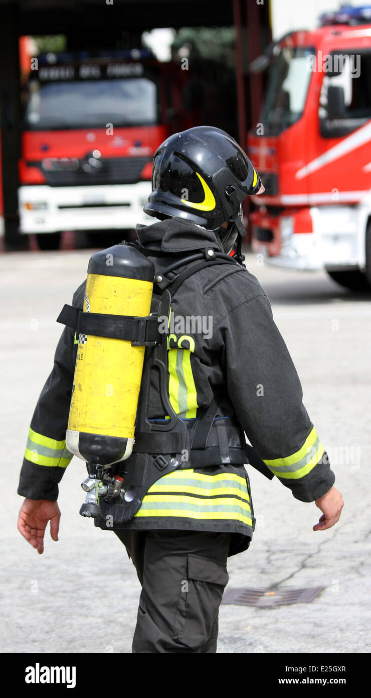 Coraggioso pompiere con giallo la bombola di ossigeno e il casco cammina verso il fuoco Foto Stock