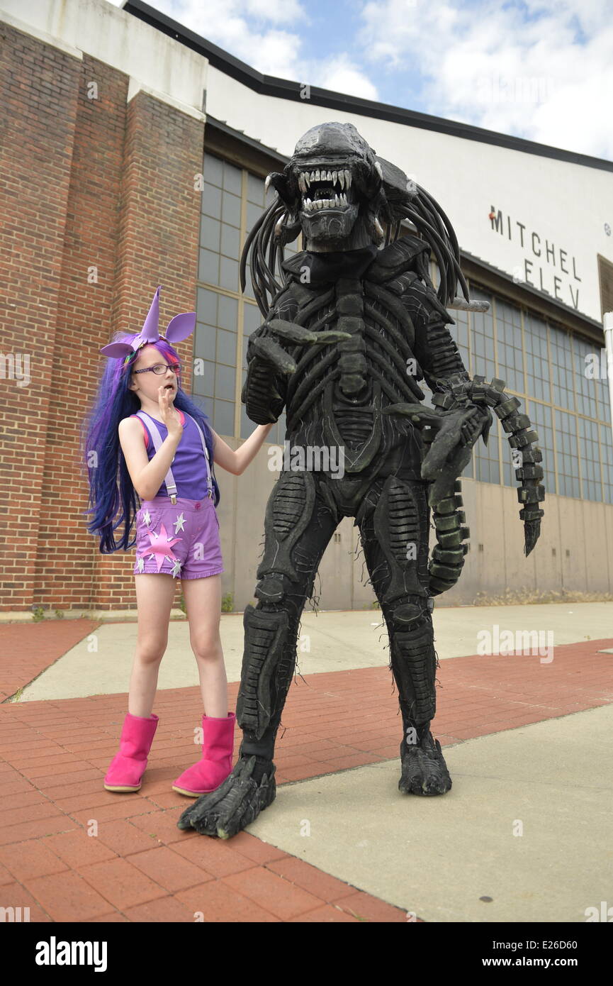 Città Giardino, New York, Stati Uniti d'America. 14 Giugno, 2014. Una giovane ragazza in un Twilight Sparkle il costume da mio piccolo Pony è con suo padre in un costume alieno, basato su Alien vs Predator movie, nella parte anteriore di uno storico campo di Mitchel hangar con eterna, annuale di Cultura Pop Expo che si terrà presso la Culla del Museo dell'aviazione sull'Isola Lunga. Credito: Ann e Parry/Alamy Live News Foto Stock