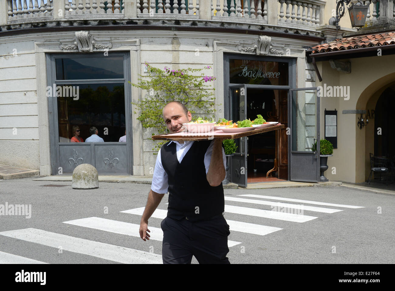 Cameriere italiano attraversamento di strada con il vassoio per alimenti Bellagio sul Lago di Como Italia / Camerieri servizio ristorante italiano Foto Stock