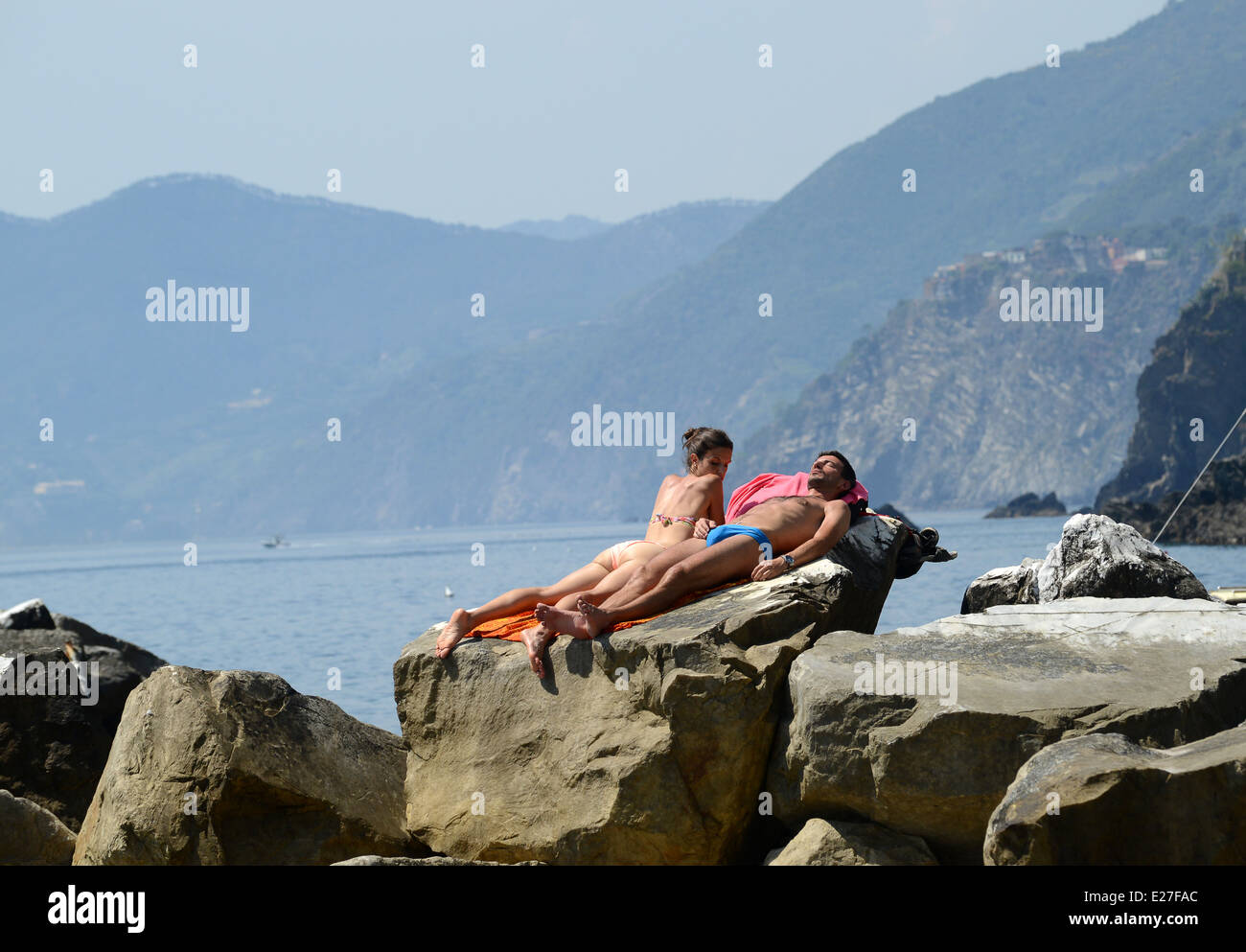 L uomo e la donna giovane a prendere il sole sulle rocce a Riomaggiore su Cinque Terre in Italia / vacanze vacanze coppie lucertole da mare Foto Stock