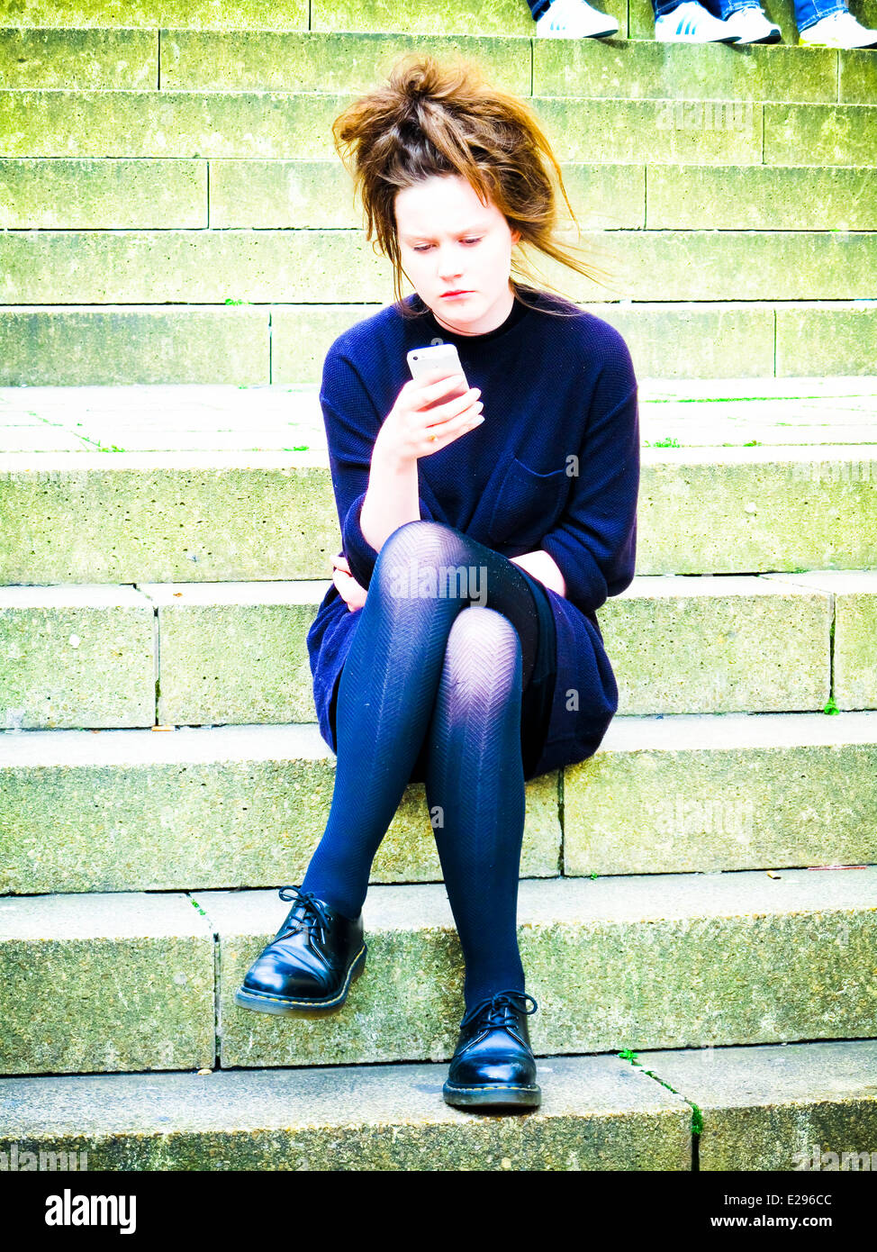 Ragazza giovane guardando telefono seduti sui gradini Foto Stock