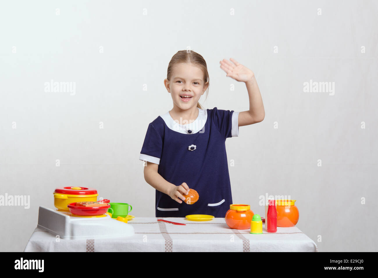 Bambina di cinque anni giocando in bambini mistress piatti a un tavolo coperto con un panno Foto Stock
