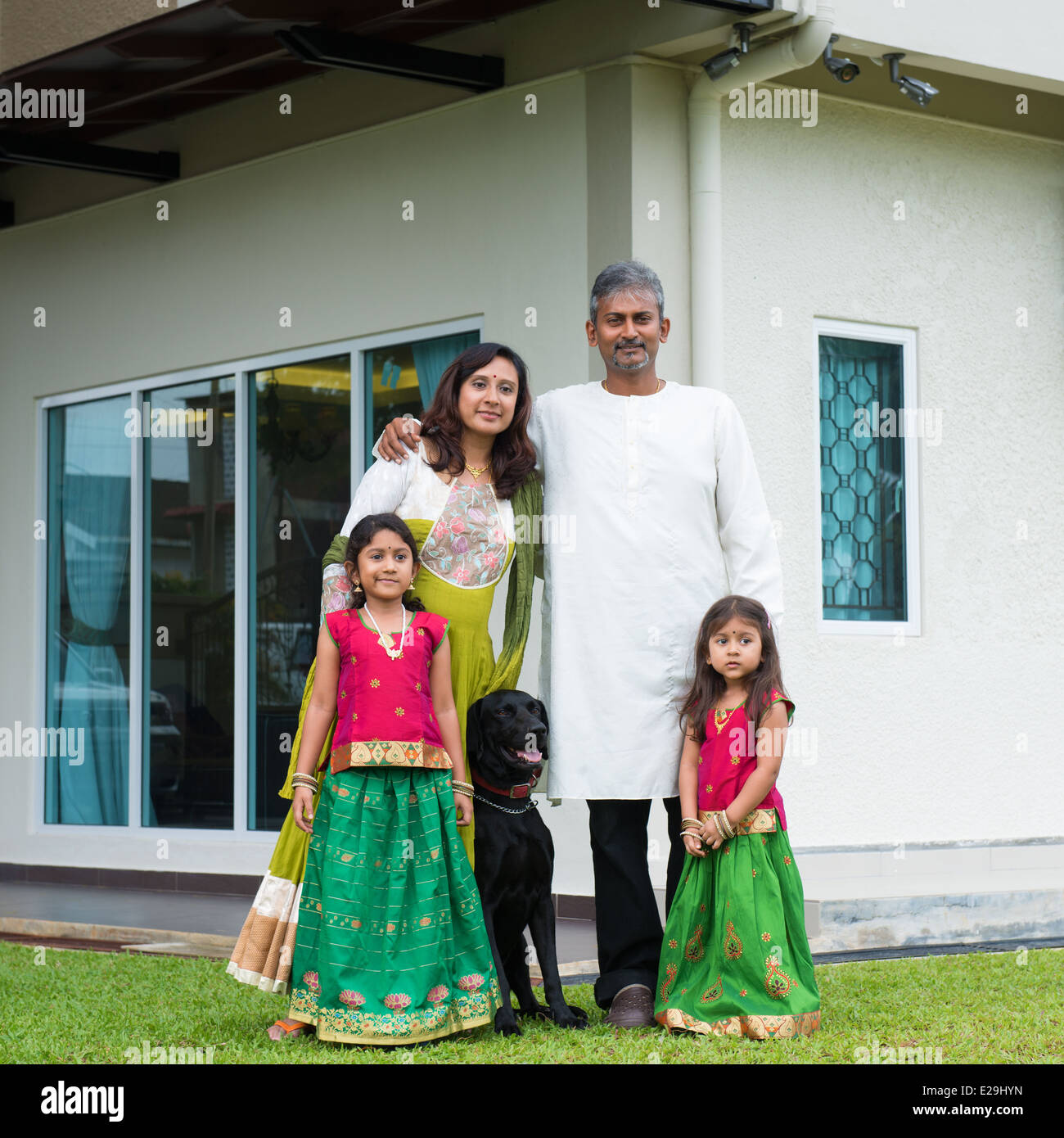 Bella asiatica famiglia indiana ritratto sorridente e in piedi al di fuori della loro nuova casa con cane da compagnia. Foto Stock