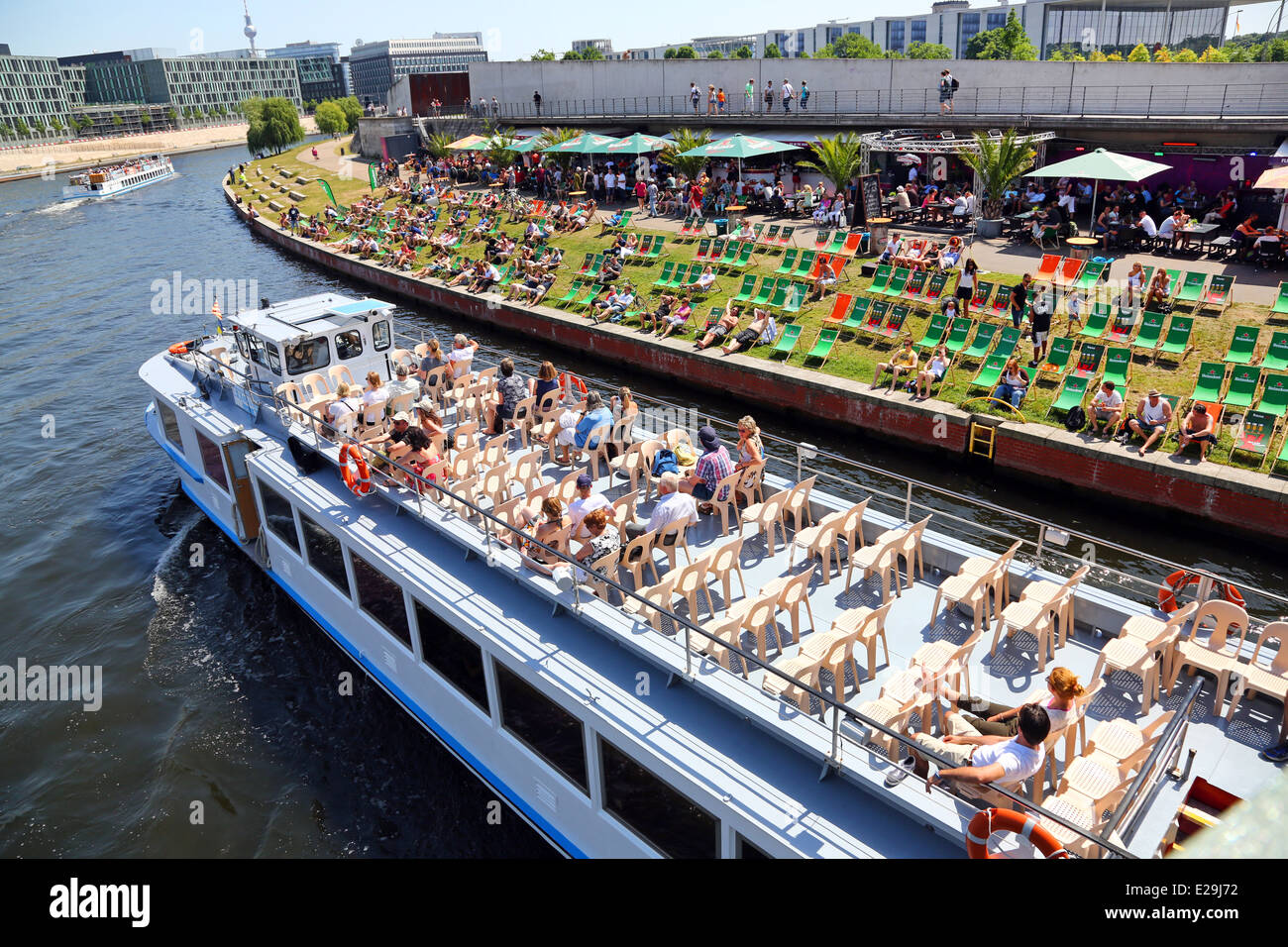 Spiaggia artificiale con sedie a sdraio vicino al fiume Sprea con un turista in barca per visite guidate a Berlino, Germania Foto Stock