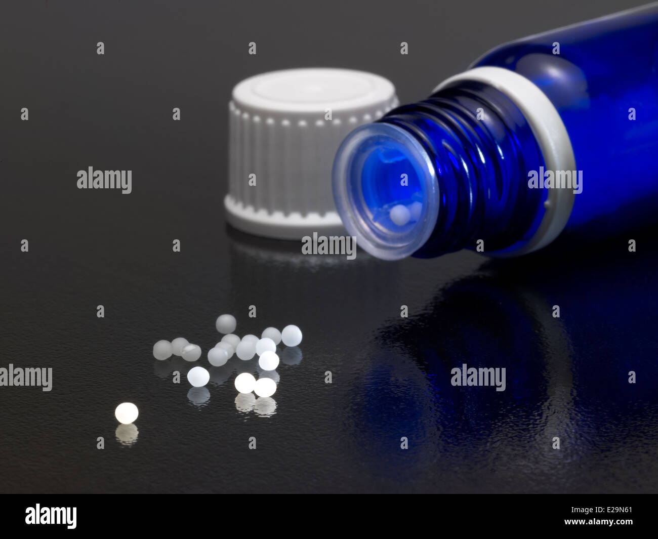 Aprire una piccola bottiglia di colore blu e il tappo sul buio massa riflettente con globuli intorno Foto Stock