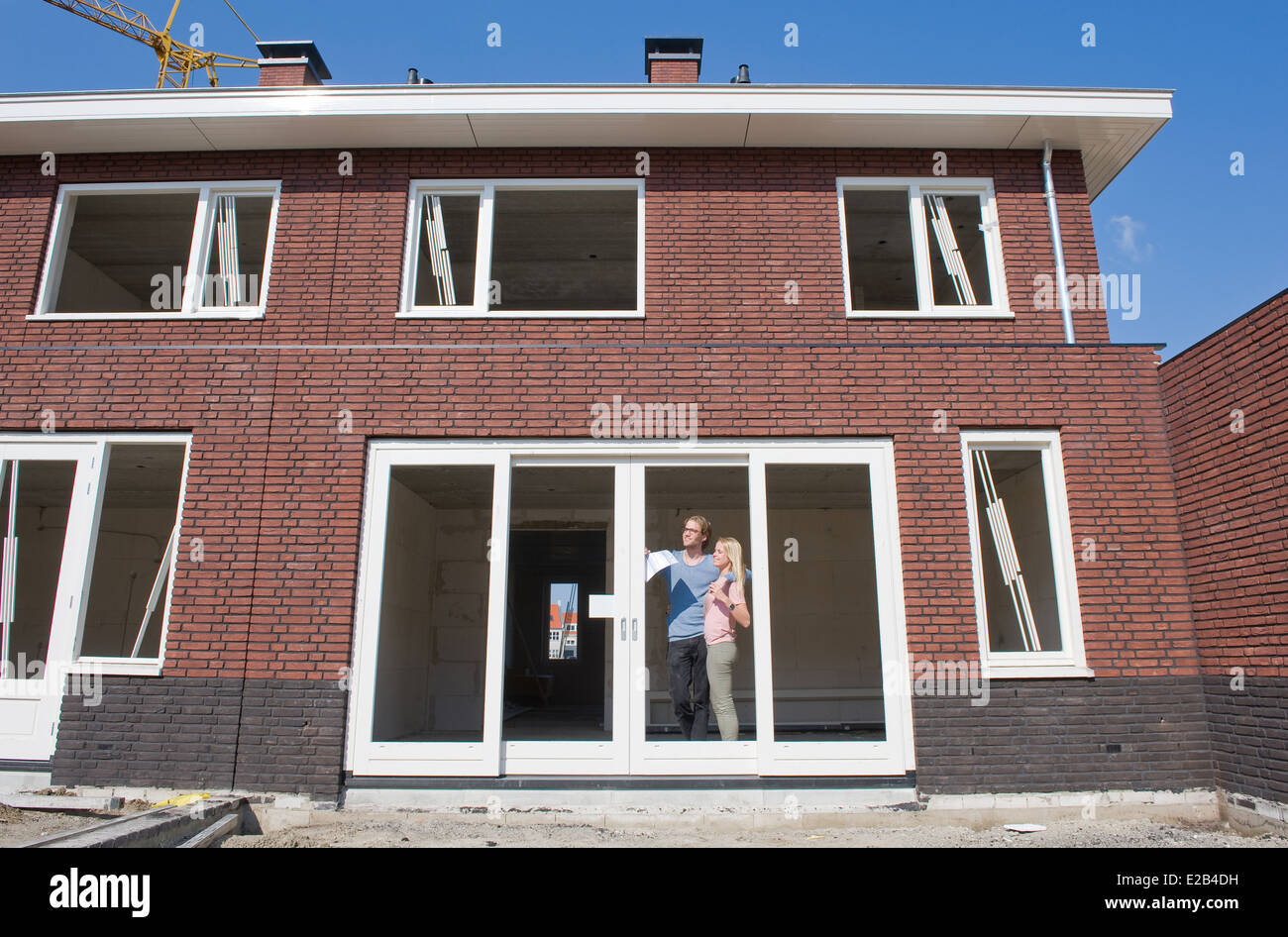 Coppia giovane con blueprint è alla ricerca felicemente al di fuori alla vista dal loro nuovo costruito home. Foto Stock