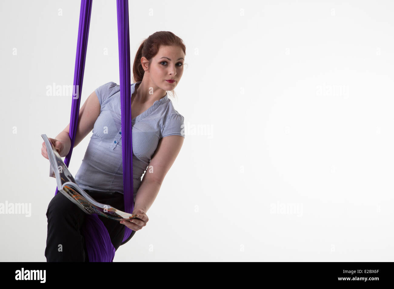 Equilibrio tra lavoro e vita privata donna sospesa dal soffitto leggendo una rivista Foto Stock