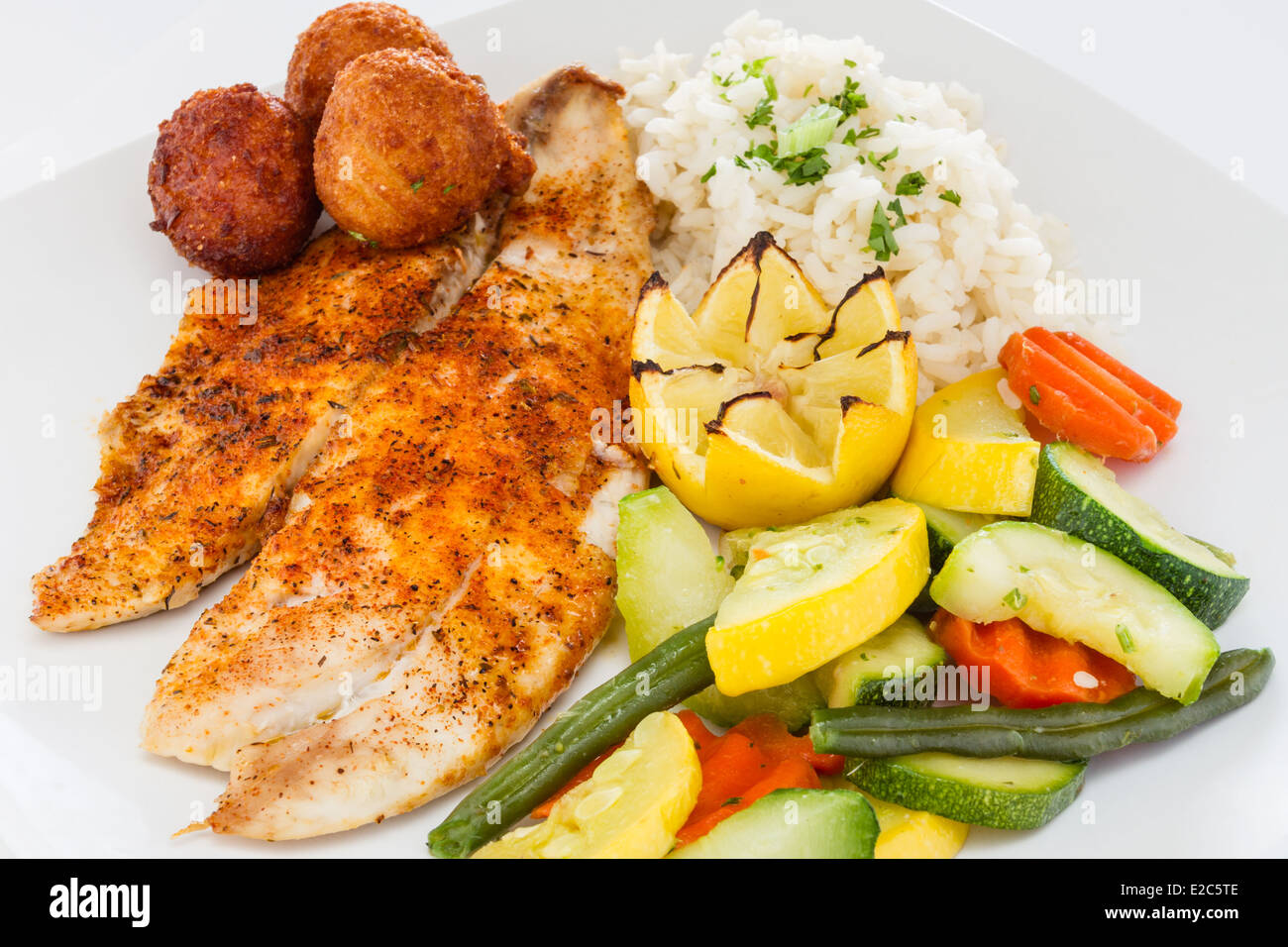 Pesce annerito servito con riso e verdure medley e frittelle di farina di mais. Foto Stock