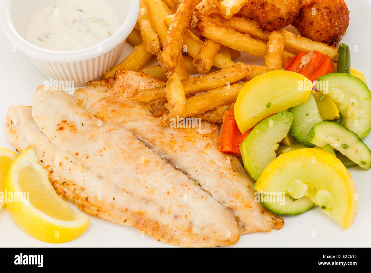 Pesce grigliato servito con patate fritte, verdure medley e frittelle di farina di mais. Foto Stock