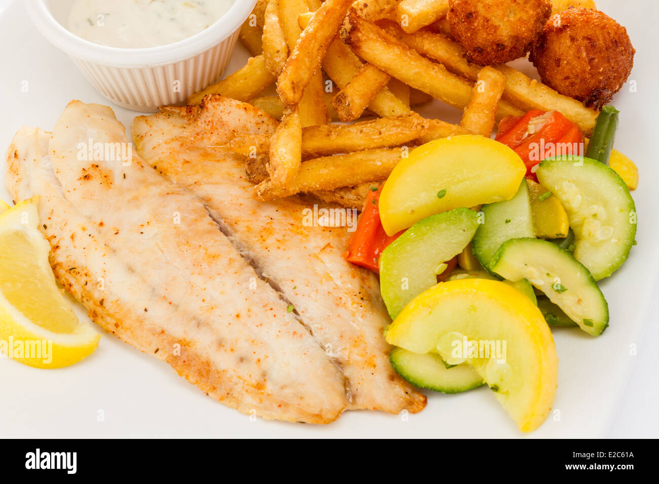 Pesce grigliato servito con patate fritte, verdure medley e frittelle di farina di mais. Foto Stock