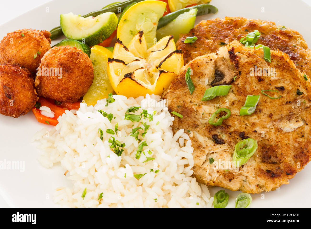 Pan fried crab cake servito con un lato di riso e verdure medley e frittelle di farina di mais. Foto Stock