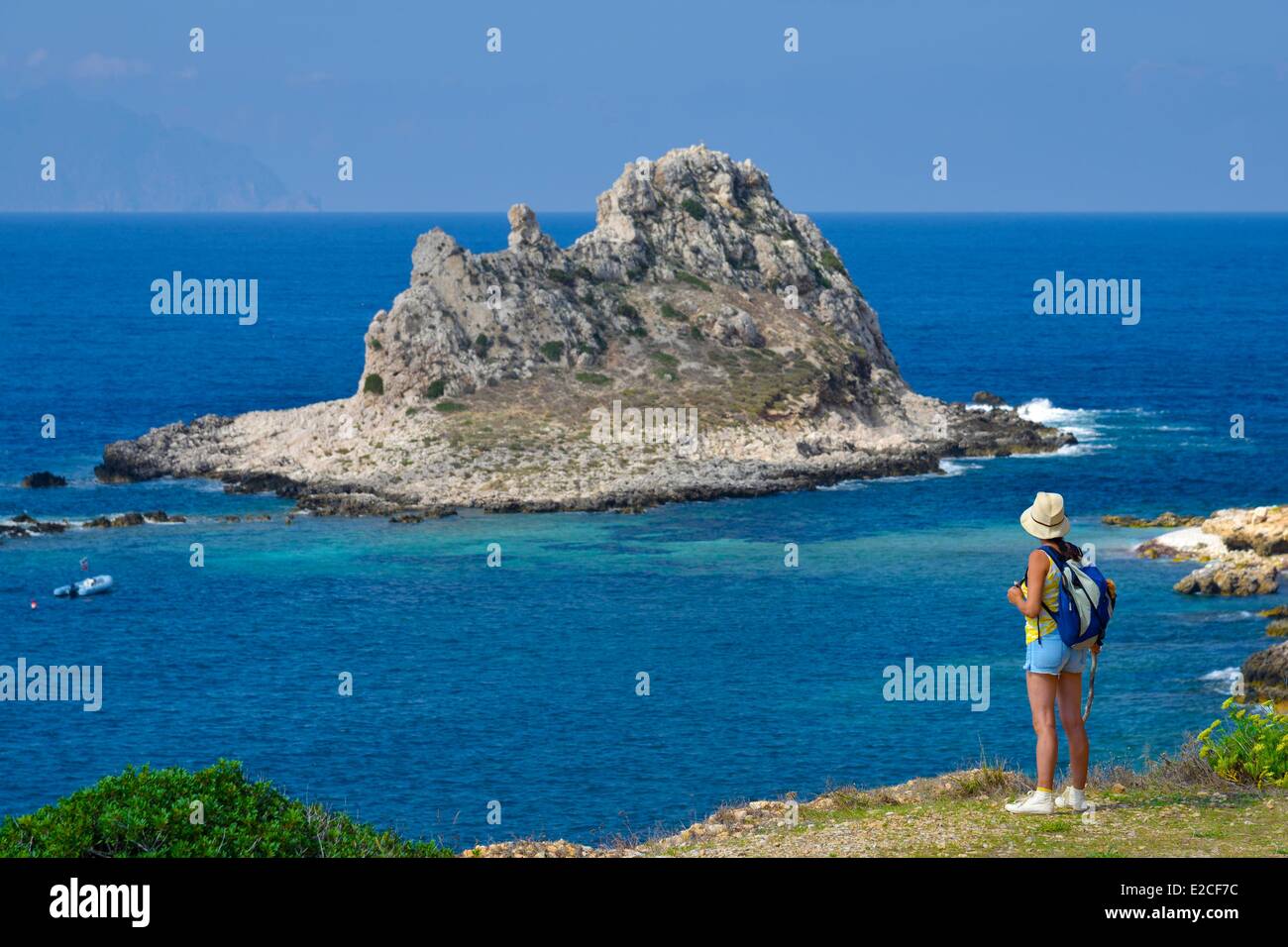 L'Italia, sicilia, isole Egadi, isola di Levanzo, escursionista su un sentiero costiero affacciato sul mare con isola Faraglione in background Foto Stock