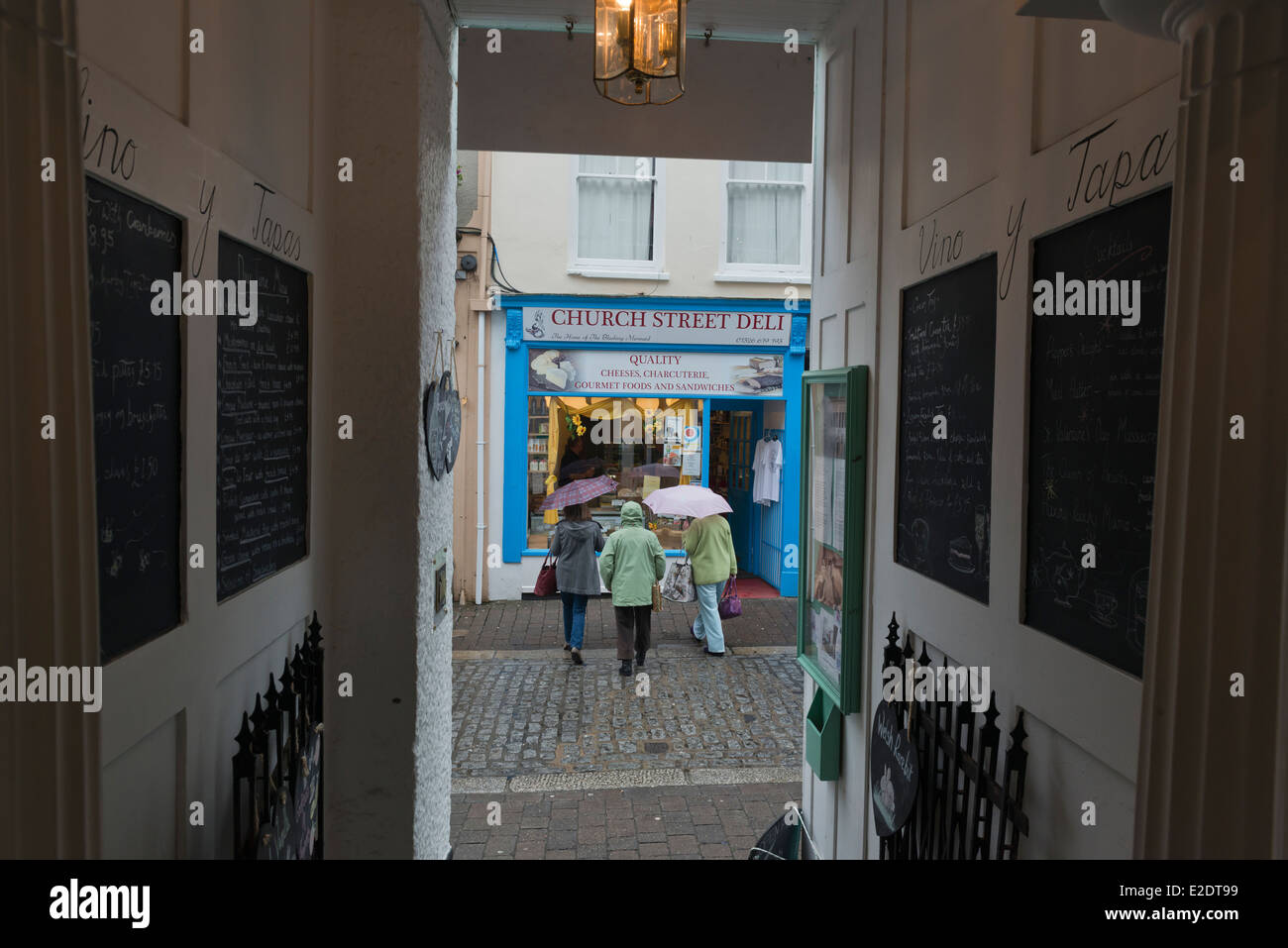 Onorevoli colleghe con ombrelloni cercando in un deli shop finestra. Falmouth, Cornwall Foto Stock