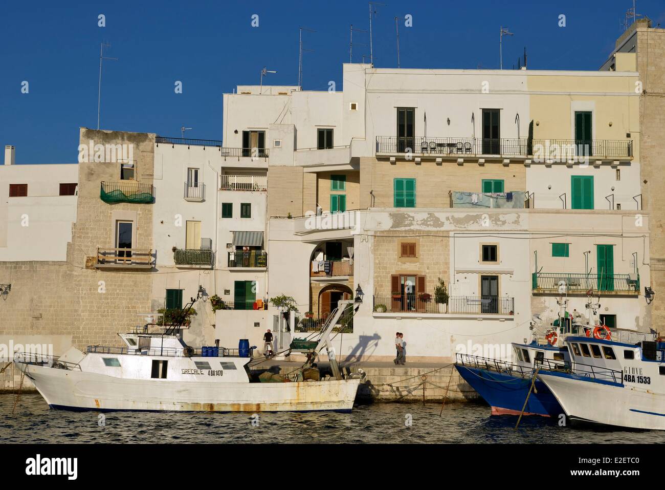 Italia Puglia Provincia di Bari, Monopoli, porto di pesca, i pescherecci con reti da traino a fianco della banchina in città al tramonto Foto Stock