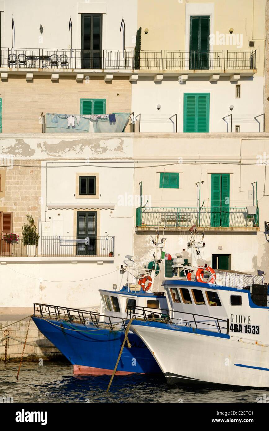 Italia Puglia Provincia di Bari, Monopoli, porto di pesca, i pescherecci con reti da traino a fianco della banchina in città al tramonto Foto Stock