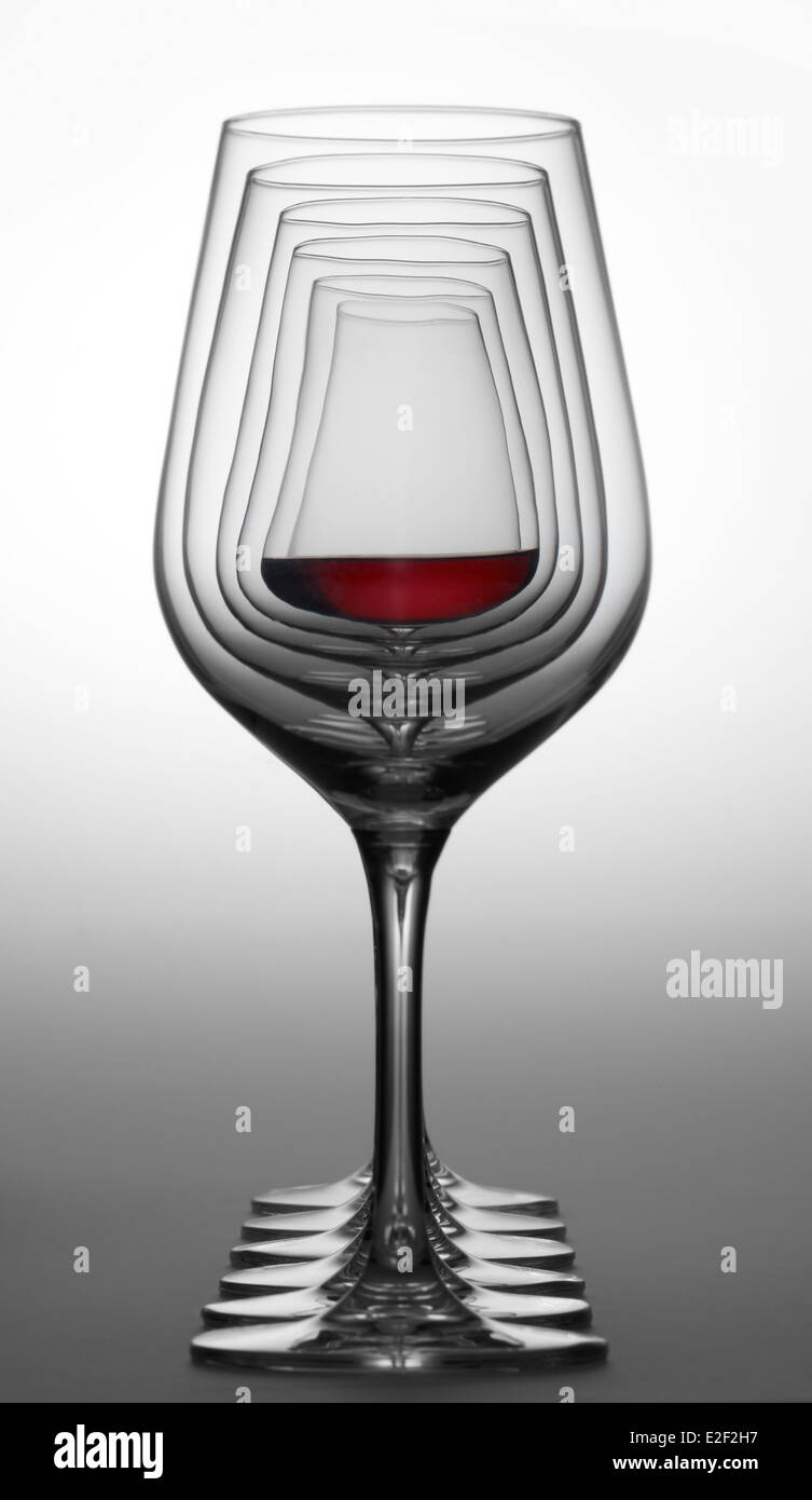 Alcuni bicchieri di vino in piedi consecutivi in una fila nel gradiente dorso grigio, uno parzialmente riempito con un bicchiere di vino rosso Foto Stock