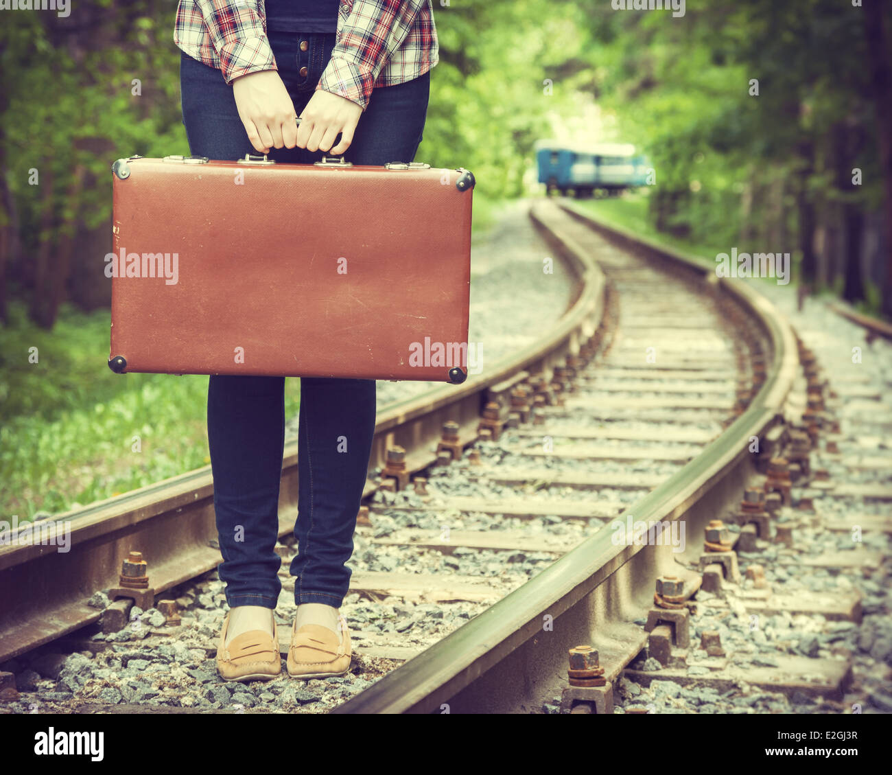 Giovane donna con la vecchia valigia su ferrovia e treno in partenza sullo sfondo, retro stilizzata Foto Stock