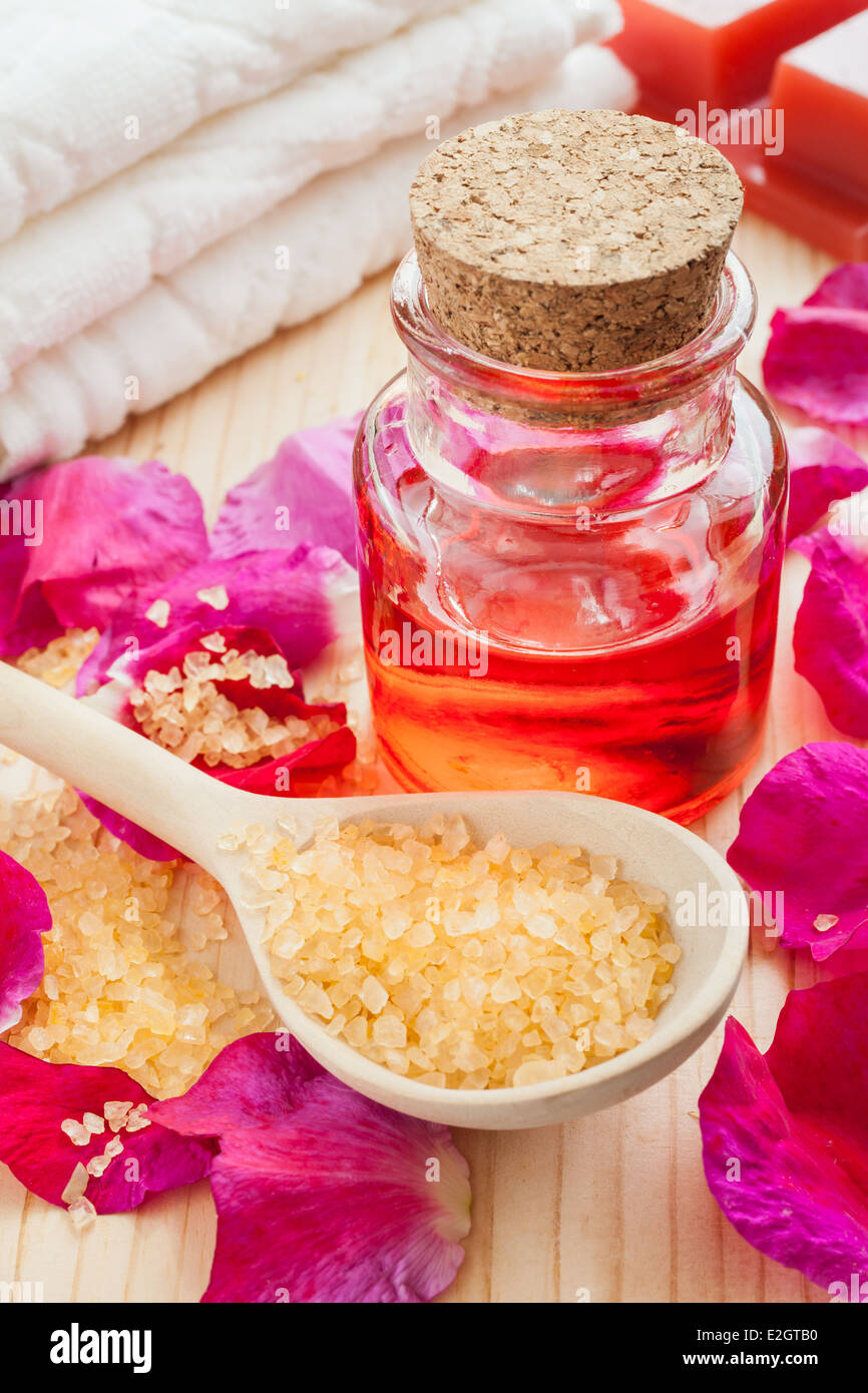 Olio essenziale in una bottiglia di vetro, sale marino, asciugamano e petali di rosa Foto Stock